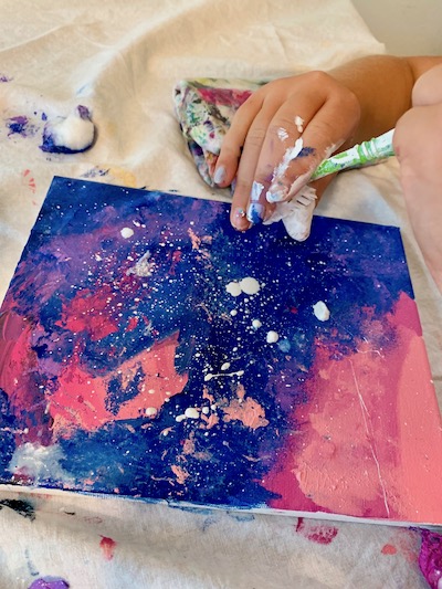 Use white paint on the tooth brush to "splatter" paint over the canvas.  Adding water to the brush first makes for a better consistency.